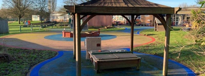 Playsmart’s Jungle Mulch bonded rubber mulch used on a playground in blue and sand-coloured rubber mulch colours in a circular pattern under a gazebo shelter